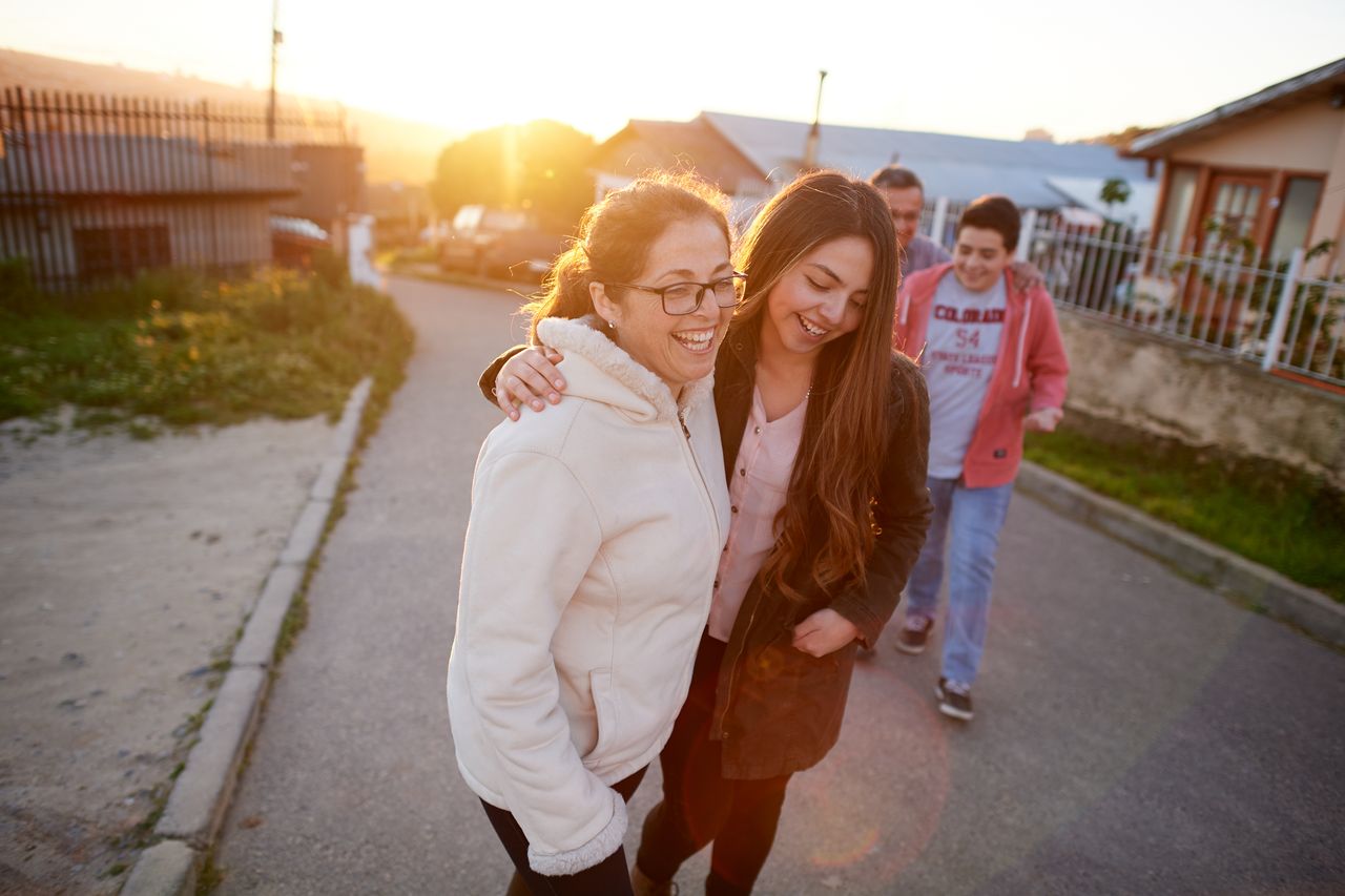 O familie tânără merge pe un trotuar bucurându-se de timpul petrecut împreună.