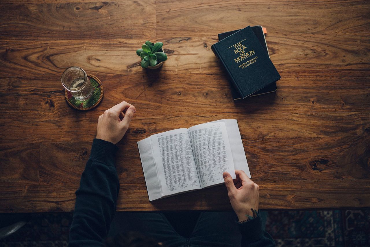 Un bărbat studiază Biblia și Cartea lui Mormon la masa din bucătăria sa.