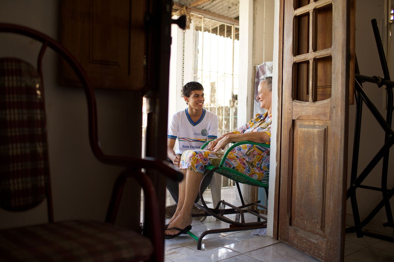 Un tânăr stă pe o verandă cu o femeie mai în vârstă în timp ce petrec timp împreună și se bucură de Evanghelia lui Isus Hristos.